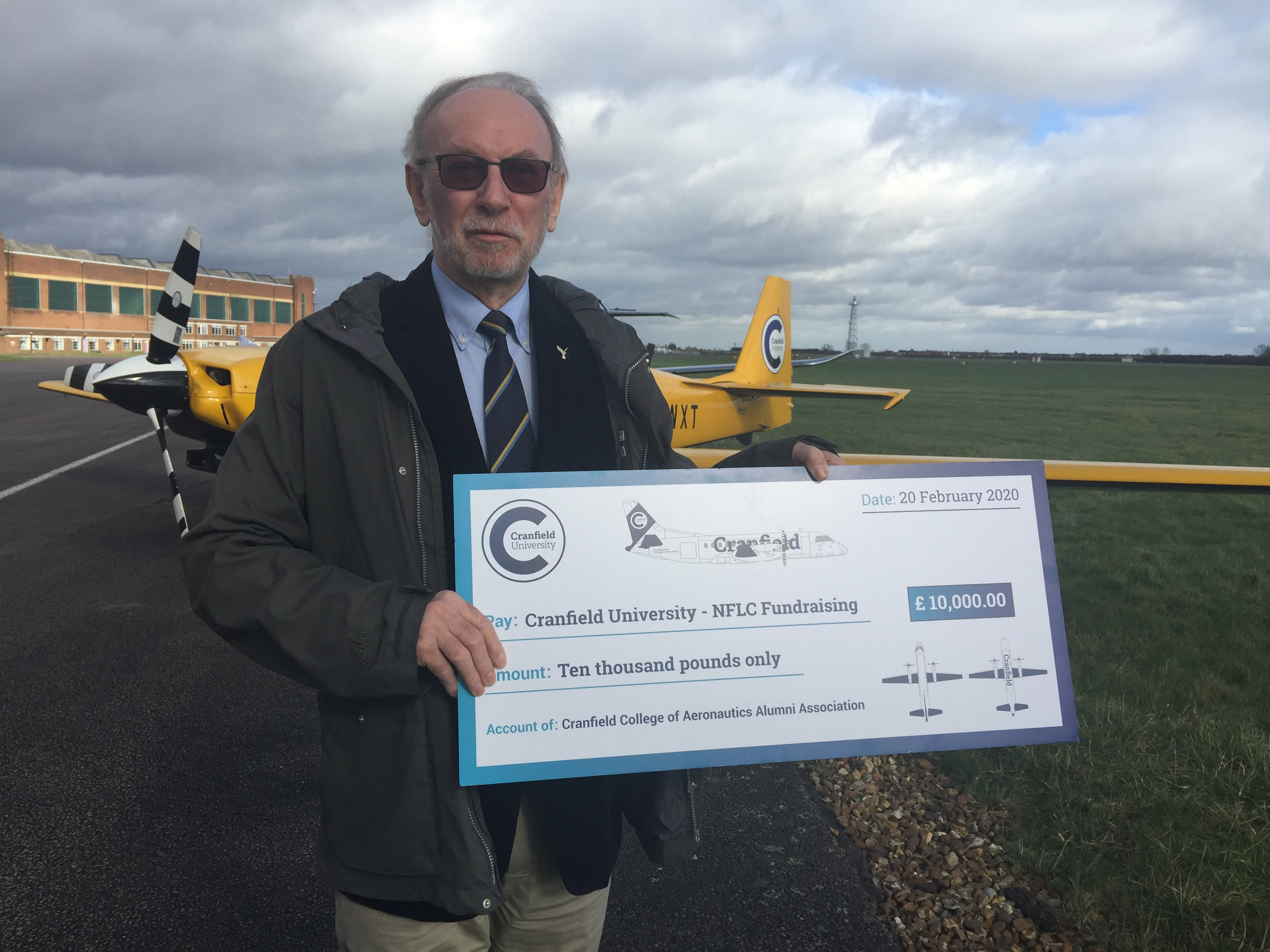 Prof John Fielding on the airfield with cheque
