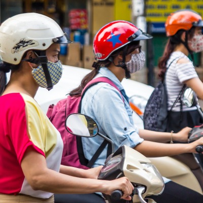 Three girls on scooters wearing helmets and masks